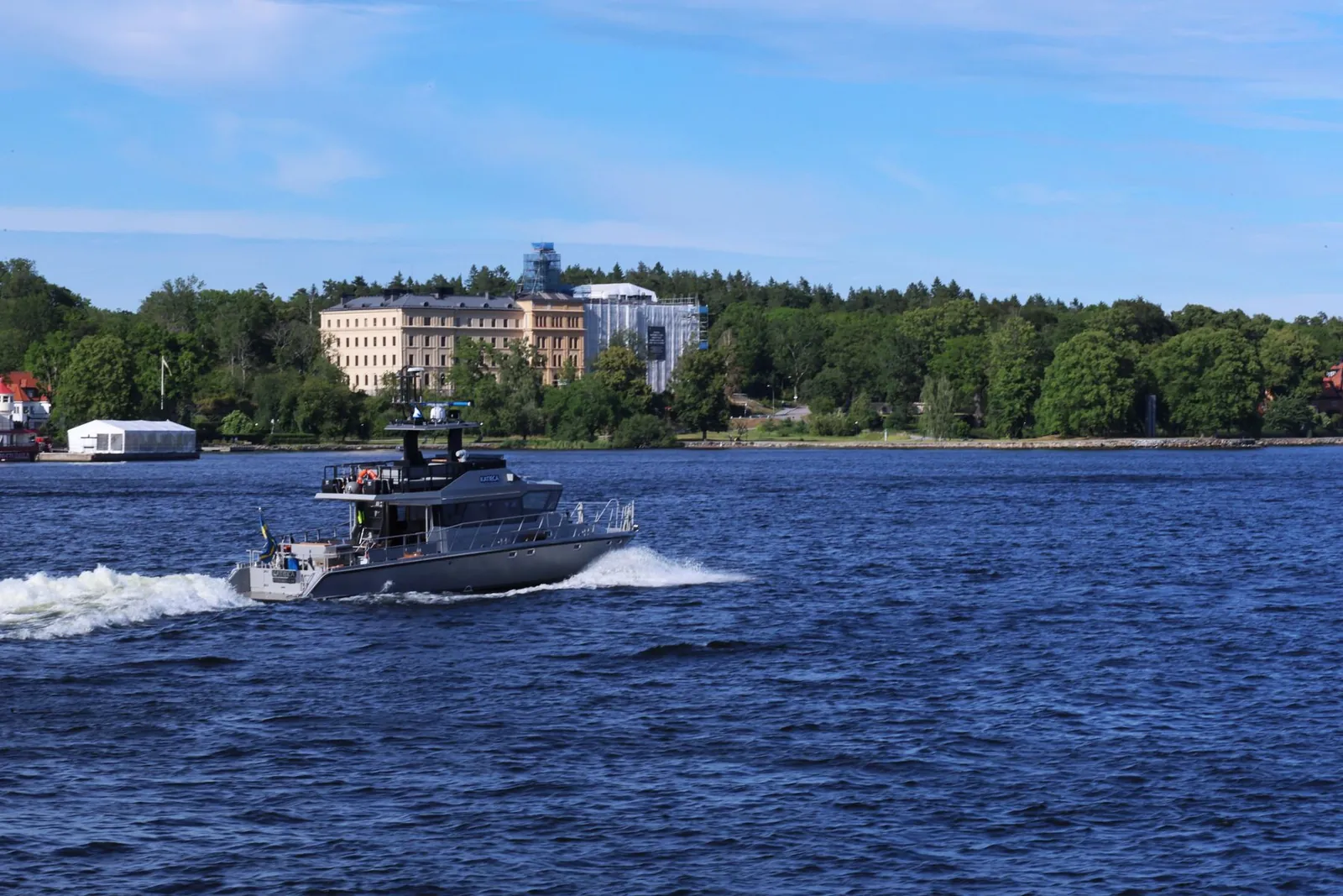 Båt på blått vatten med grönskande öar och bebyggelse vid Stockholm